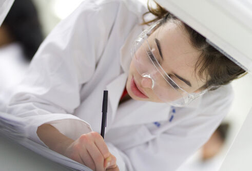 Student in white coat in lab at a machine
