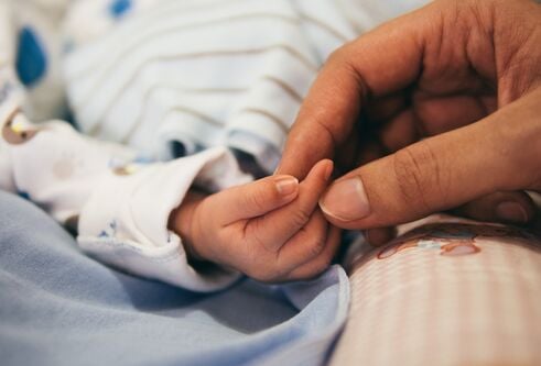An adult holding a baby's hand