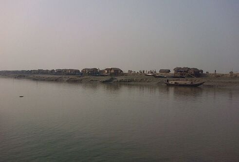 grey looking river with traditional houses alongside it in Bangladesh
