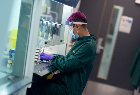 Person in green boiler suit facing left, working at scientific piece of equipment