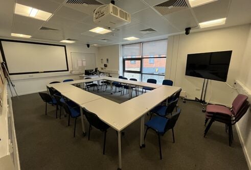 Dalhousie 2F02 - tables set in an oblong with chairs. A mobile tv screen and a white screen on the wall