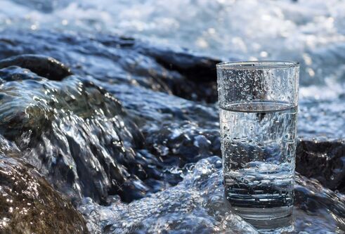A glass of water sitting on a rock in a river.