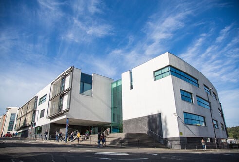 A large white building with blue sky and students walking in the foreground