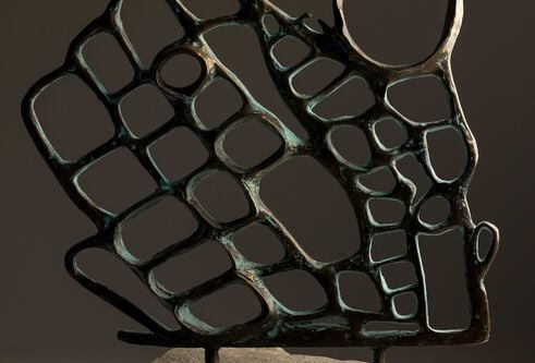 Sculptural metal piece with holes and spikes on a stone pedestal.