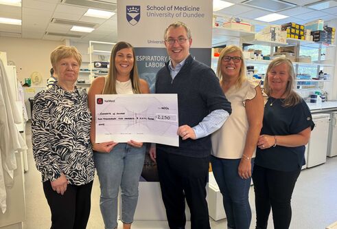 Five people stand together holding a large sized cheque.