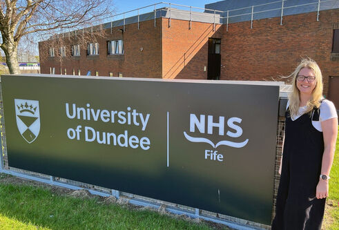 A woman standing in front of a large NHS and UoD sign outside