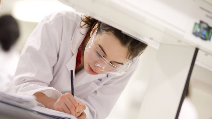student working in lab in a lab coat, writing with a pen