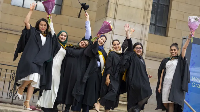 A group of women wearing academic robes at the University of Dundee's Winter Graduation raising their hands and bouquets of flowers as they cheer