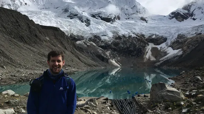 Man standing at the top of a mountain, with a pool of glacier water behind him