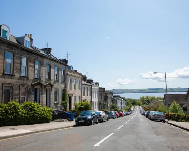 Street with older style buildings and cars parked along the kerb, road leading down to sea at end of street