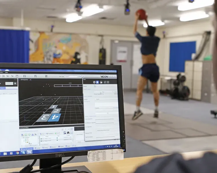 A man throws a basket ball inside a lab while another person watches on a computer that monitors his movement