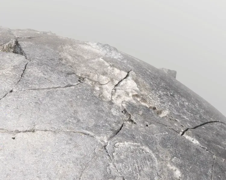 A section of a grey concrete looking sphere, against a pale grey background.