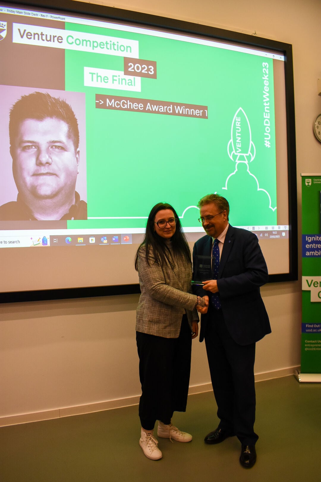 A woman shaking hands with a man, standing in front of a projector screen.