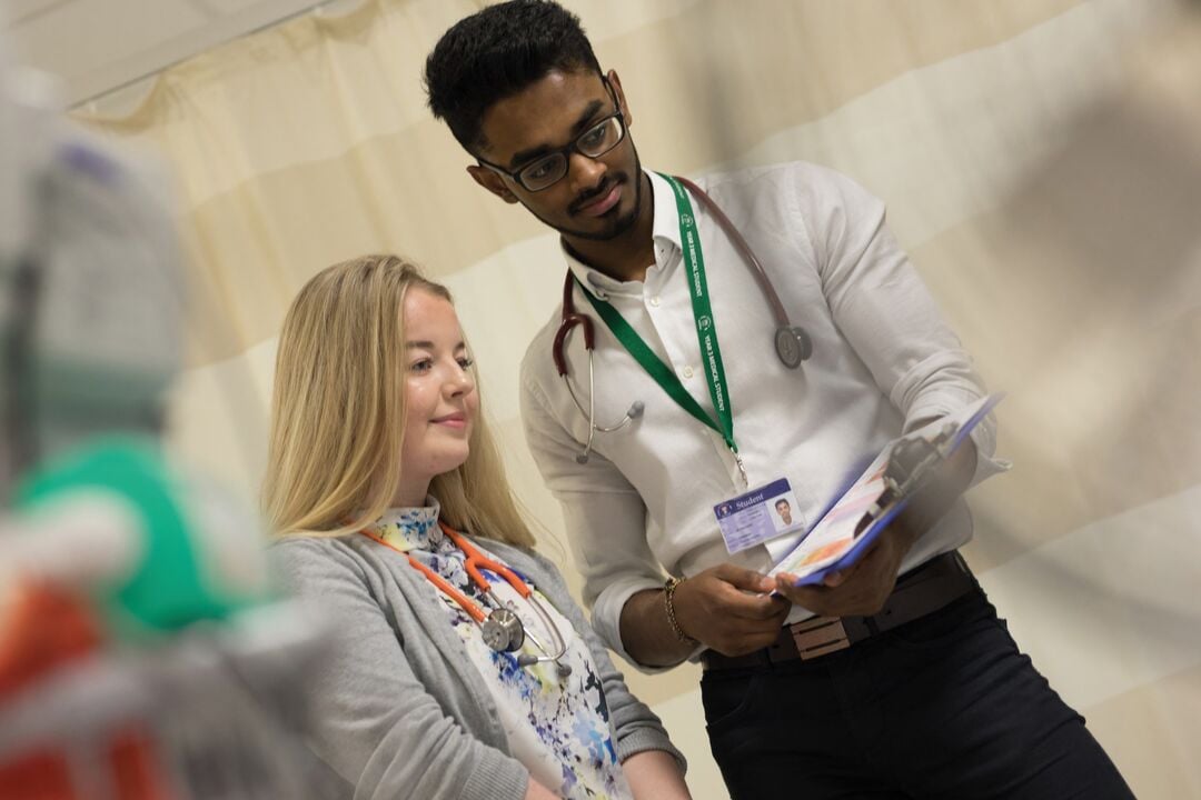 A medical student shows information on a clipboard to a fellow student