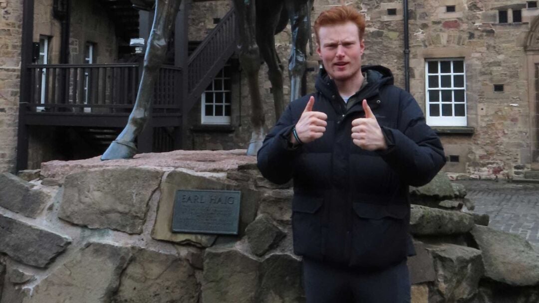 Jarrett Fiske stands with two thumbs up standing beside a statue of a horse