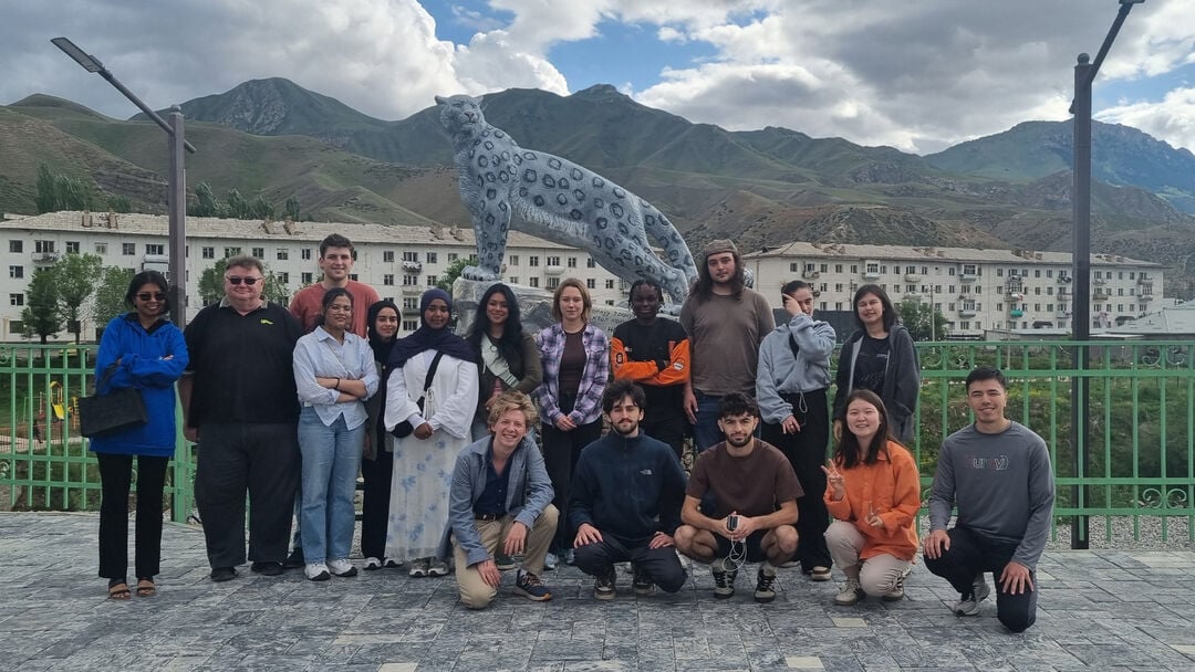 A large group of students, standing in a line smiling at the camera, standing outside mountains behind them and a statue of a cheetah 
