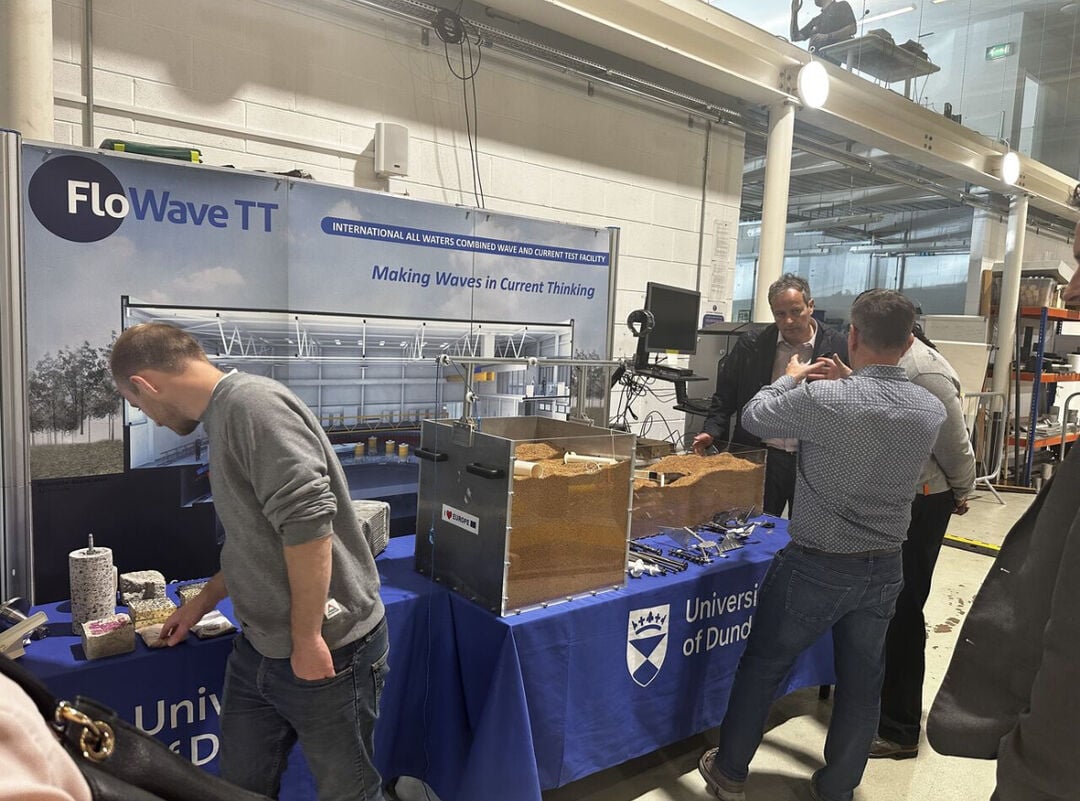 tables with University of Dundee branded table cloth hanging down from them and large glass tank on top of them, filled with sand and small machinery inside.