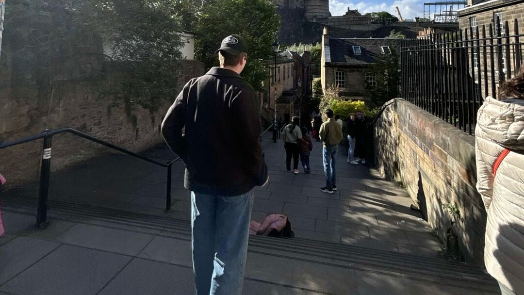 Student walking down a flight of stairs with stone walls and buildings on either side
