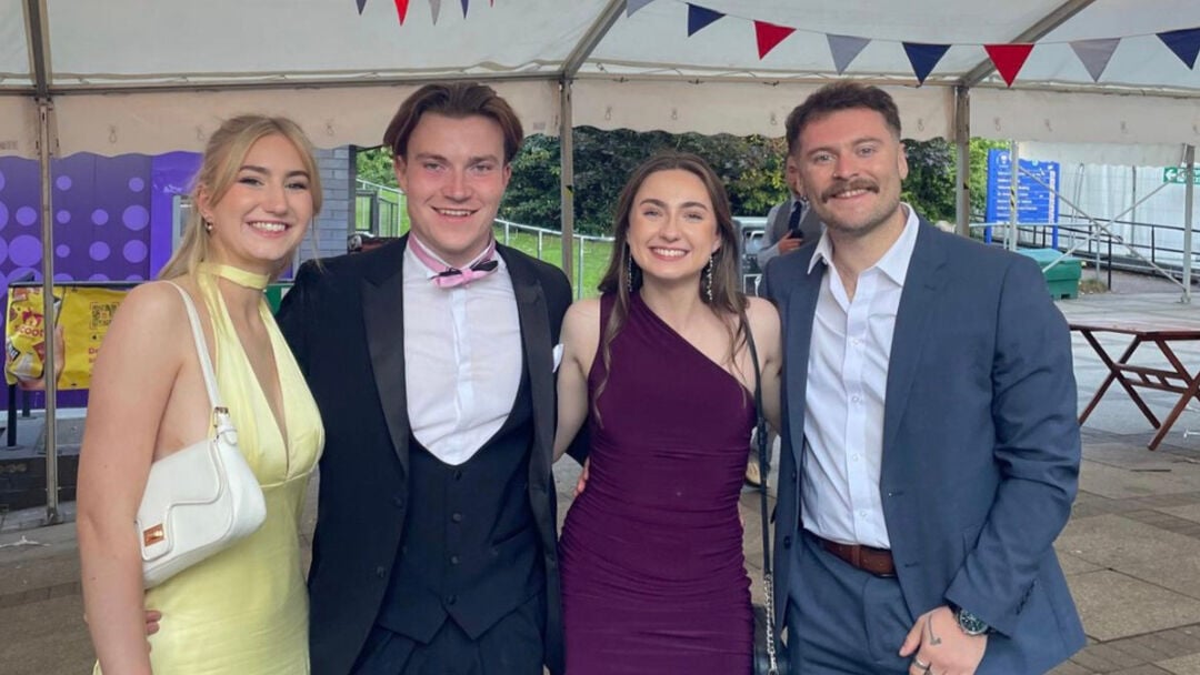 4 students standing together posing for the camera in smart wear in a tent on graduation